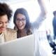 Implementing employee engagement ideas and programs can help boost morale, as represented by this image of two women celebrating success while looking at a laptop.